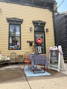 Exterior of Artmarkit in Covington, Kentucky, featuring a yellow storefront, outdoor seating with a checkered table, and a sidewalk sign advertising it as a creative reuse hub.