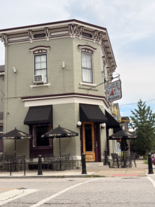 Exterior of The Crazy Fox Saloon in Newport, Kentucky, showing its historic corner building with patio seating and black Tito’s-branded umbrellas.