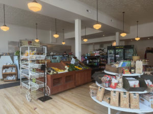 Interior of Reka’s butchery and market, showing displays of fresh produce, Italian groceries, dry goods, and a refrigerated case labeled Fresh Food. Wooden floors, pendant lights, and organized shelves create a clean and welcoming shopping space.