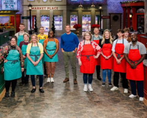 Contestants from Season 12 of Food Network’s Holiday Baking Championship pose together on the show’s festive holiday kitchen set.