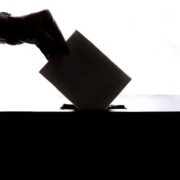 A person's hand submitting a vote into a ballot box. Voting Rights.