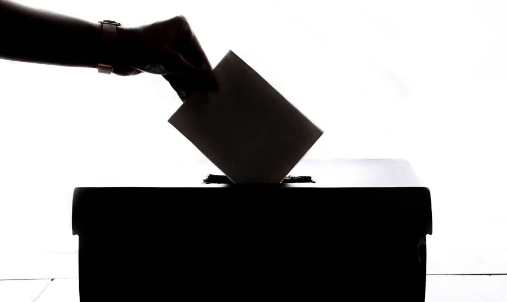 A person's hand submitting a vote into a ballot box. Voting Rights.