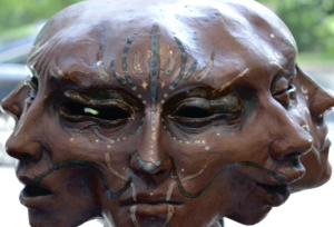 A close-up of a glazed ceramic sculpture by Murry Foust featuring three conjoined faces with hollow eyes, intricate blue and white painted markings, and a dark brown glaze, displayed at the Cincinnati Art Museum pop-up gallery.