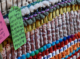 A close-up of a green handwritten tag on the colorful community loom that reads, "Rest in peace Murry… your legacy lives on through your art. You are my role model for wanting to pursue art as a trans man myself."