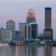 The Louisville, Kentucky skyline reflected in the Ohio River at dusk, with the illuminated dome of the Jefferson County Courthouse visible at center.