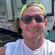 Nathan Wilson smiling in sunglasses and a neon cap in front of a Matthew25 mobile health clinic truck