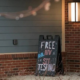 The exterior entrance of AVOL Kentucky, Suite 100, photographed at dusk. A black A-frame chalkboard sign in front of the brick and gray-sided building reads "Free AVOL HIV STI Testing" in colorful lettering. String lights hang above the entrance, and bare winter shrubs line the base of the building.