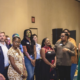 A group of LGBTQ+ community leaders and organizers stand together in a ballroom at the downtown Louisville Marriott during the Creating Change 2027 kickoff event. A person in a lavender blazer speaks into a microphone on the left while the group listens. A presentation screen is partially visible in the background. Attendees wear name tags and represent a diverse range of backgrounds and organizations from across Kentucky and the country.