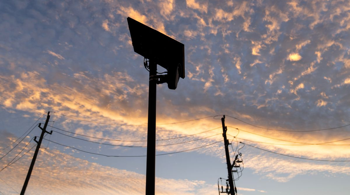 A Flock Safety automated license plate reader camera silhouetted against a sunset sky, part of a surveillance network that raises particular privacy concerns for LGBTQ+ people in Northern Kentucky.