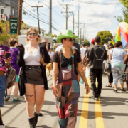 Attendees stroll down a street lined with tents and vendors at a Pride festival in Louisville's Tyler Park neighborhood, passing an ice cream stand and a rainbow-colored art installation