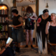 A group filled with smiles and love gathers in a home filled with books and decor.