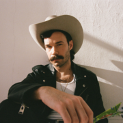 Queer country and Lavender Cowboy singer-songwriter Andrew Sa in a promotional photo, wearing a white cowboy hat and black leather jacket.