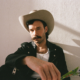 Queer country and Lavender Cowboy singer-songwriter Andrew Sa in a promotional photo, wearing a white cowboy hat and black leather jacket.