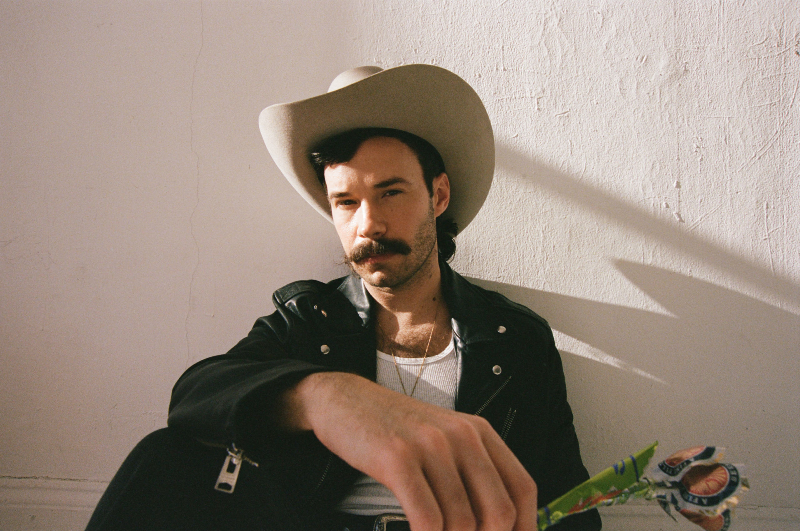 Queer country and Lavender Cowboy singer-songwriter Andrew Sa in a promotional photo, wearing a white cowboy hat and black leather jacket.