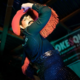 Seymour Hiney performs at a Smoke & Queers queer burlesque show in a sequined outfit with red fringe, arms raised on stage.
