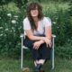 S.G. Goodman sits in a folding lawn chair in a field of wildflowers, wearing a white T-shirt, black wide-leg jeans and black boots.