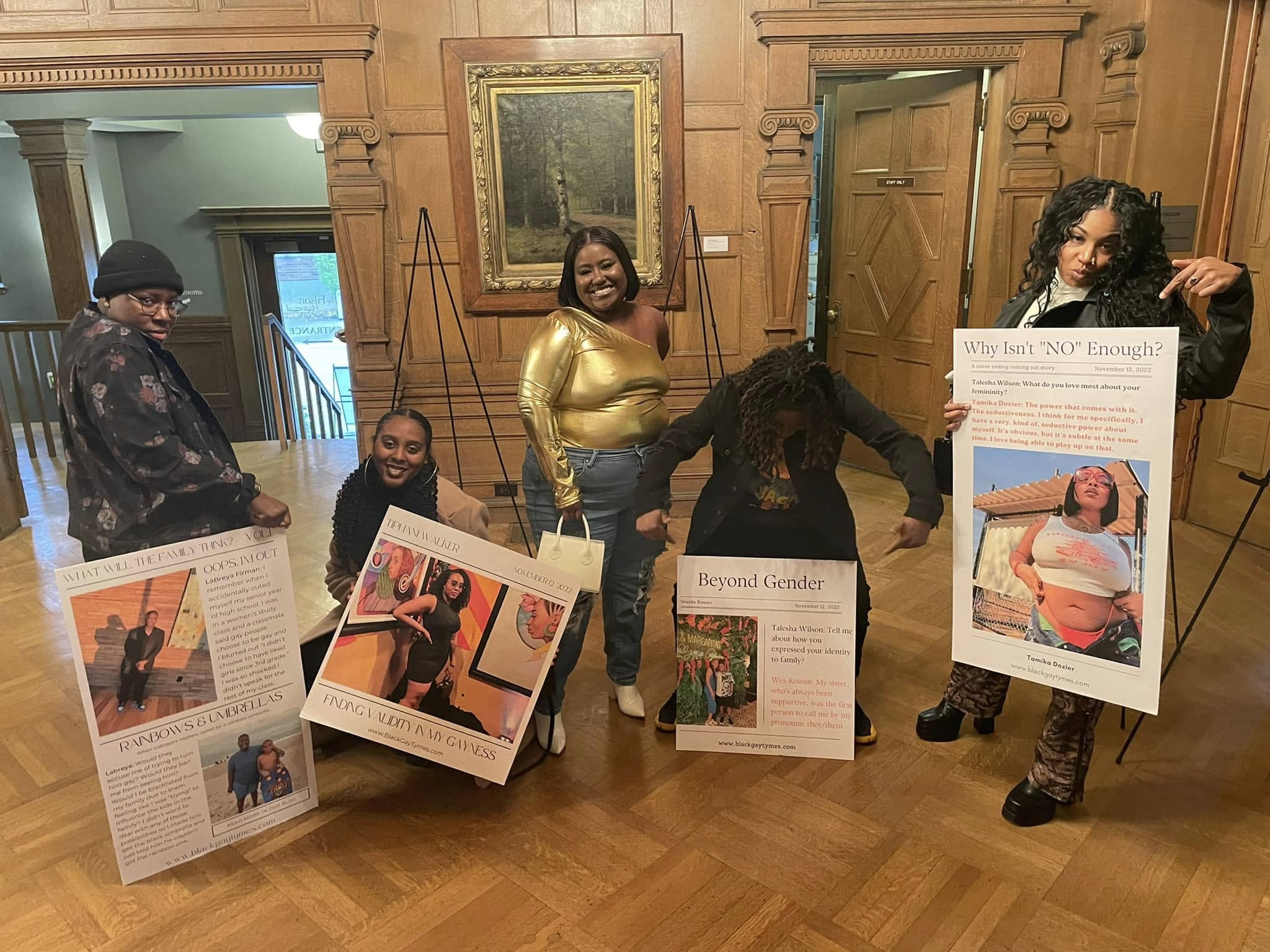 Five people pose in a wood-paneled room with poster boards from an exhibit, including boards titled "Beyond Gender" and "Why Isn't NO Enough?"