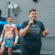 Missy Spears speaks into a microphone at an outdoor event, with drag performers standing behind her.