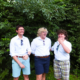 Seth Rane, Grayson Castellucci and Eddy Risimini, three students in white button-down shirts, laugh together in front of a wall of green leaves.
